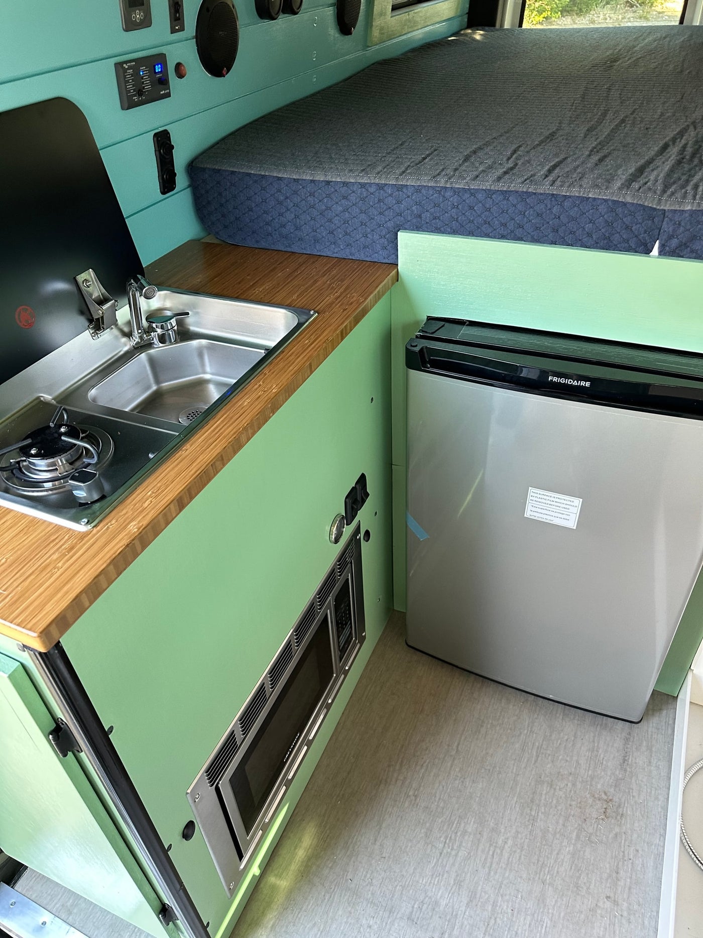 RV rental interior showcasing a modern kitchen with stove, sink, and microwave, plus a compact fridge and cozy bed. — photo 10
