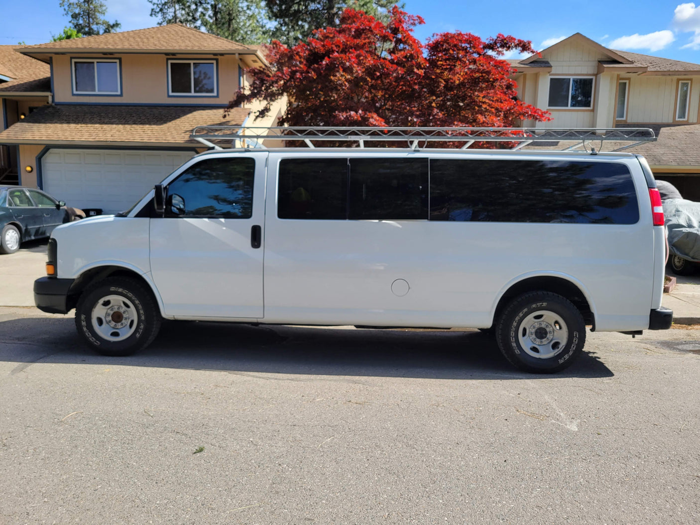 White commercial van with roof rack, potentially for rv rental; parked by homes & a vibrant red tree.