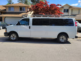 White commercial van with roof rack, potentially for rv rental; parked by homes & a vibrant red tree.