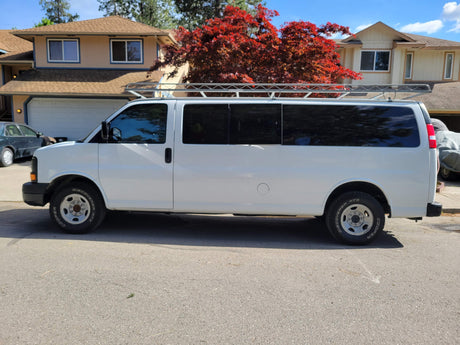 White commercial van with roof rack, potentially for rv rental; parked by homes & a vibrant red tree.