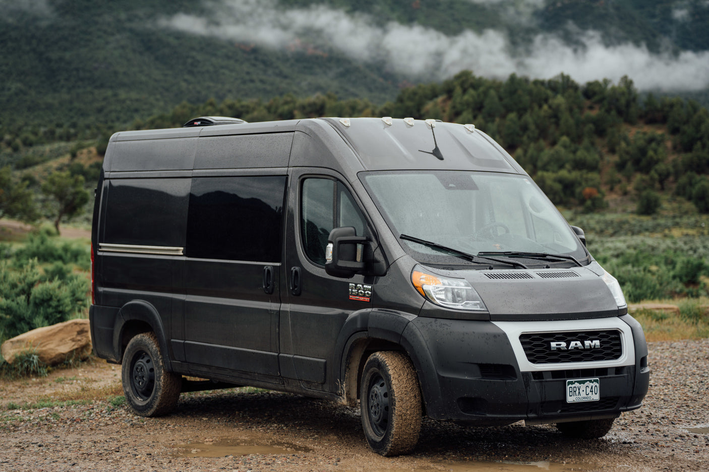 Explore Colorado's mountains in this rugged grey camper van, an ideal RV rental for off-road adventures on muddy roads.