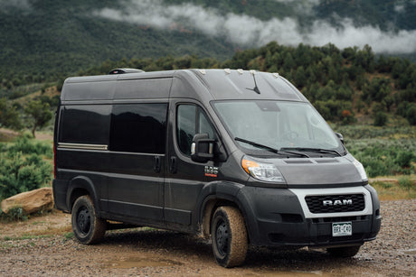 Explore Colorado's mountains in this rugged grey camper van, an ideal RV rental for off-road adventures on muddy roads.