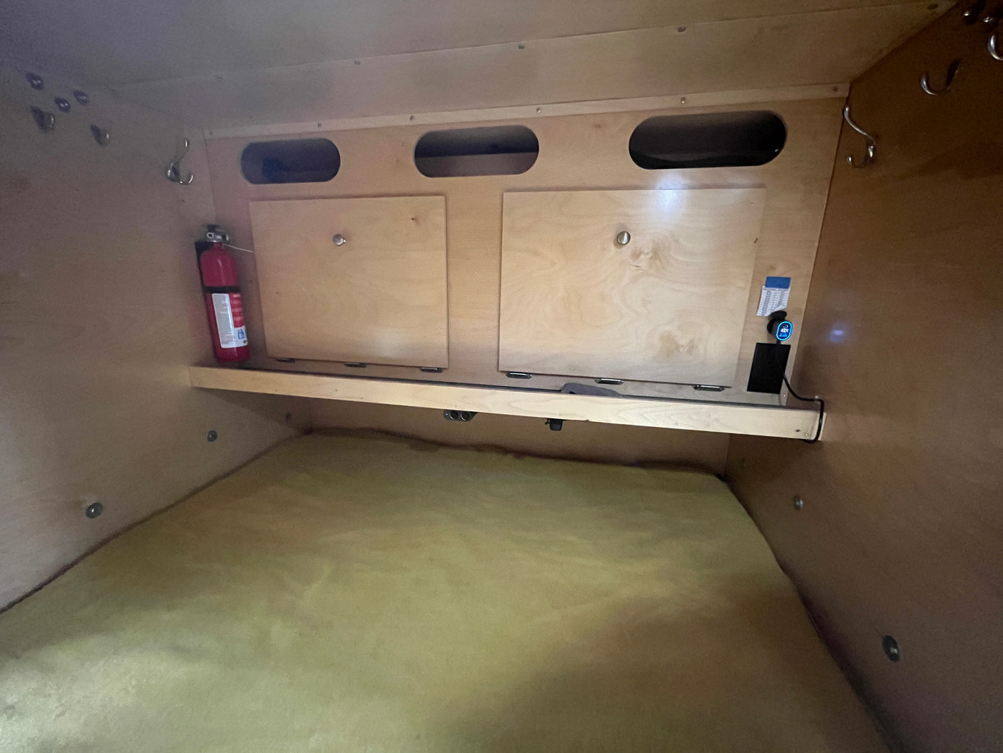 RV rental interior: Compact sleeping area with mattress, storage, fire extinguisher, and power access.