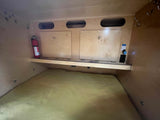 RV rental interior: Compact sleeping area with mattress, storage, fire extinguisher, and power access.