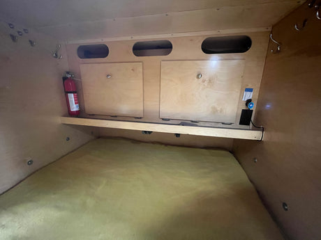 RV rental interior: Compact sleeping area with mattress, storage, fire extinguisher, and power access.