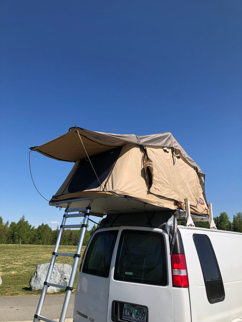 This RV rental features a white van with a deployed tan rooftop tent and ladder, ready for outdoor adventure under a clear blue sky. — photo 4