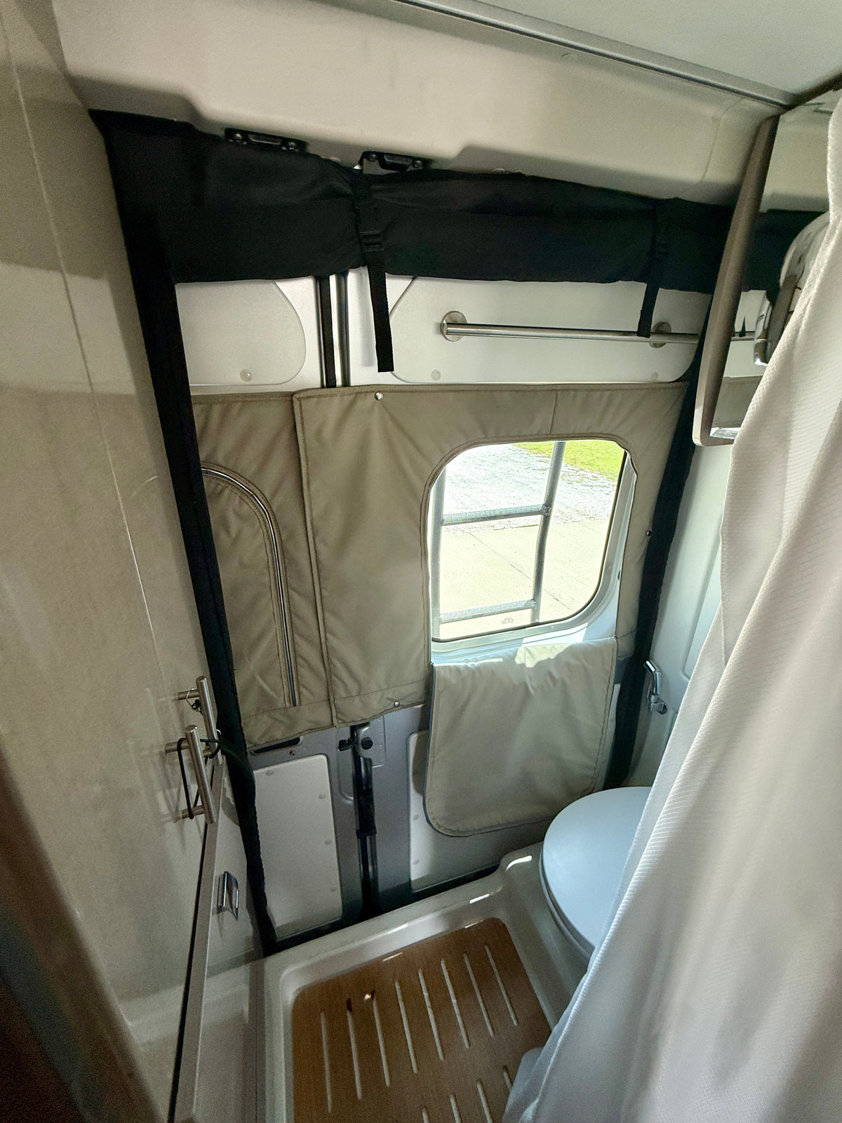 Explore this compact RV rental wet bath, featuring a toilet, shower pan with wooden mat, and curtain, viewed through an open door. — photo 9