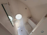 RV rental bathroom: compact toilet, shower, mirror, and ceiling vent in a small, white, self-contained space.