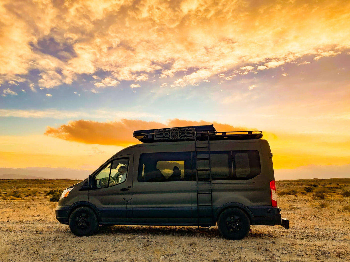 Adventure awaits! Dark grey RV rental camper van parked in the desert at sunset with vibrant orange clouds. — photo 6