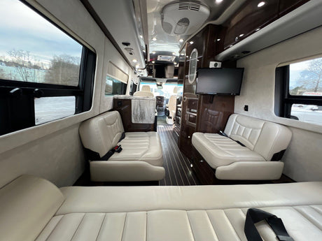 Spacious luxury RV rental interior with cream leather seating, wood accents, and entertainment system.