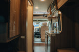 Interior of an RV rental: kitchenette with sink, wood cabinets, and clear view to the driver's seat, perfect for road trips.