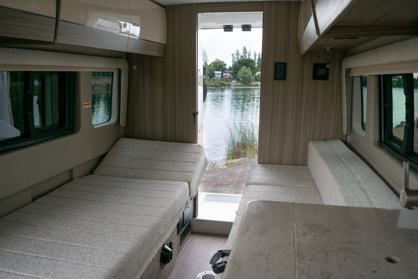  maximizing small space utility.|Stay powered up in your RV rental! This modern interior features a pop-up power outlet with USB ports for convenient device charging.|Dark grey camper van (RV rental) parked lakeside with open side door showing interior — photo 8