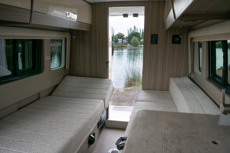  maximizing small space utility.|Stay powered up in your RV rental! This modern interior features a pop-up power outlet with USB ports for convenient device charging.|Dark grey camper van (RV rental) parked lakeside with open side door showing interior — photo 8