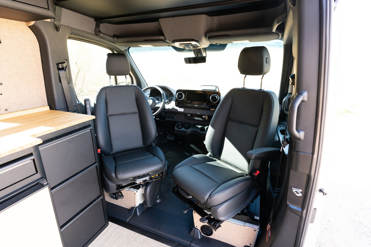Spacious RV rental interior featuring swivel front seats, dashboard, and a custom kitchenette for comfortable van life. — photo 9
