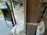 This rv rental interior features a compact bathroom with toilet, shower, and storage cabinetry, ready for adventures.