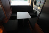 Inside this RV rental, find a compact dining area with a white table and dark cushioned benches. Perfect for travel.