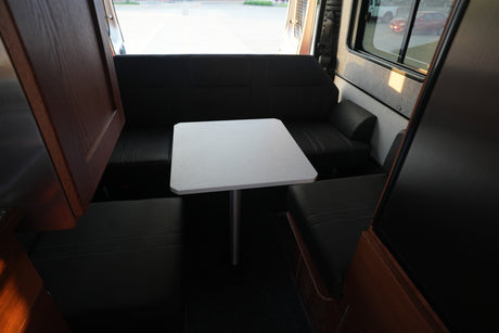 Inside this RV rental, find a compact dining area with a white table and dark cushioned benches. Perfect for travel.
