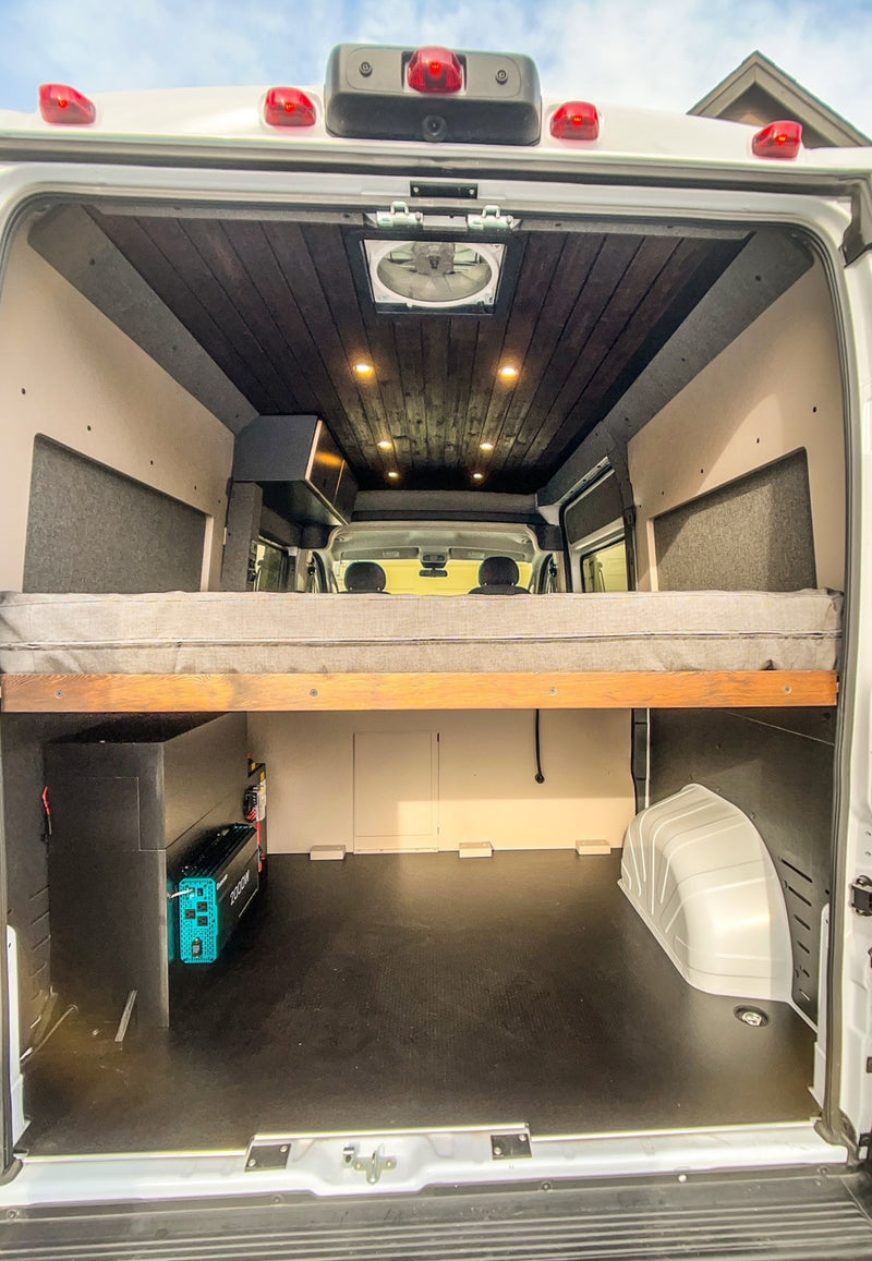 Inside this RV rental van conversion: a cozy elevated bed, sleek dark wood ceiling, and extensive lower storage with power system. — photo 6