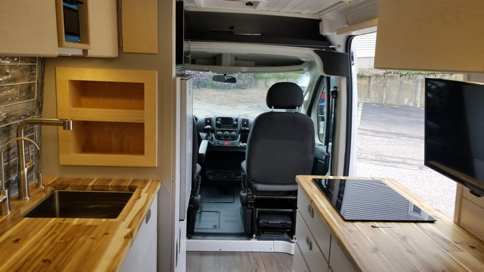  and a lush green outdoor view.|Step inside this inviting RV rental! A comfy camper van interior featuring blue seating