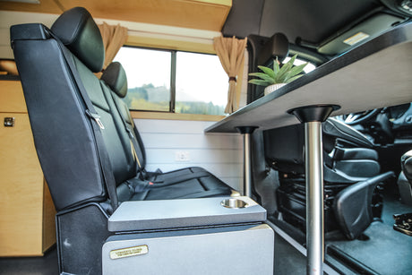 RV rental: Bright campervan interior with black seats, a dining table, and a versatile cooler that converts to a bed.