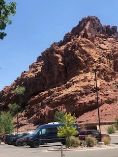 Dark RV rental in a parking lot, backed by a towering red rock mountain under a bright blue desert sky. — photo 18