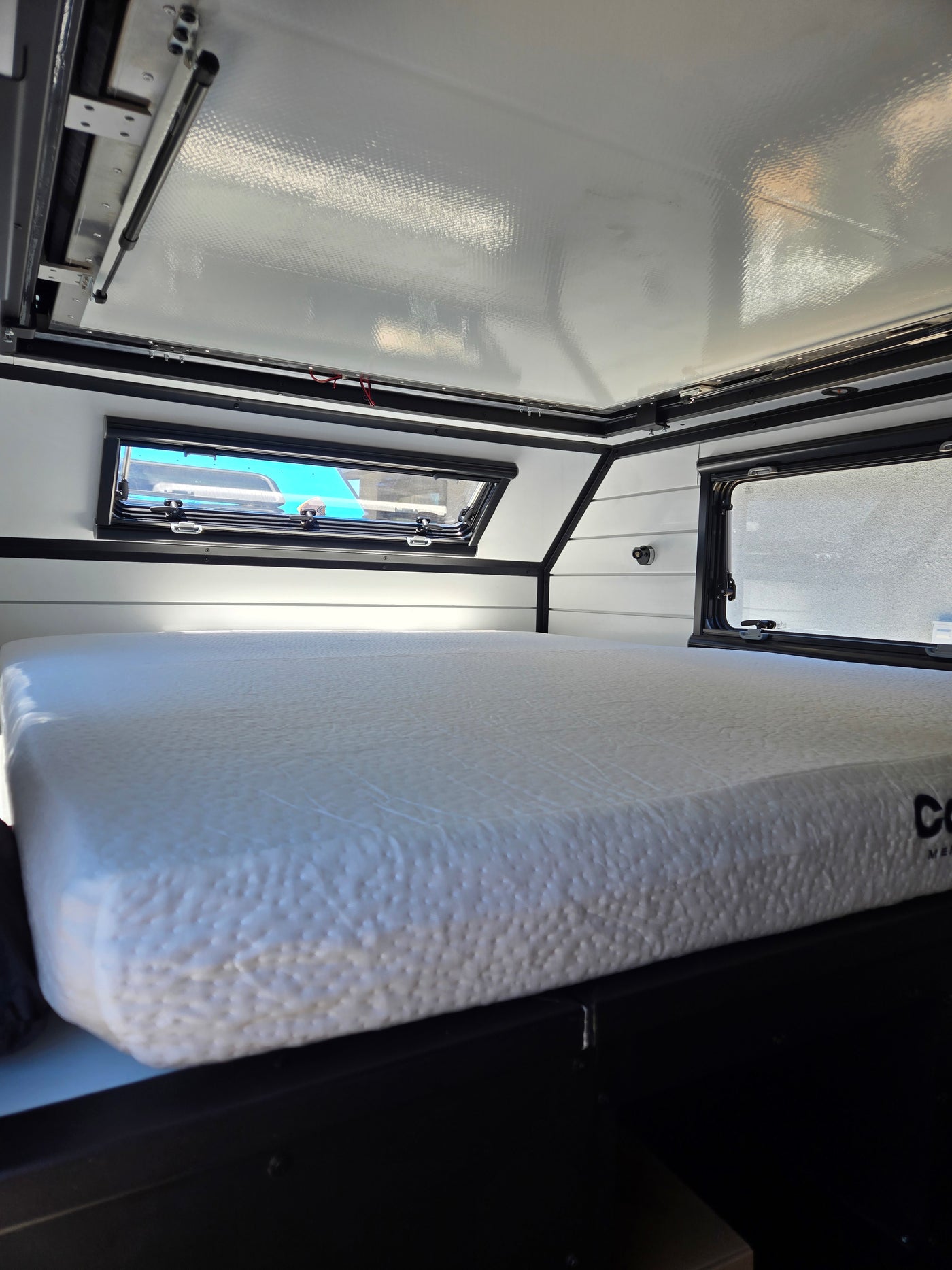 Compact RV rental sleeping area with textured mattress, large windows & pop-top roof, ready for adventure. — photo 6