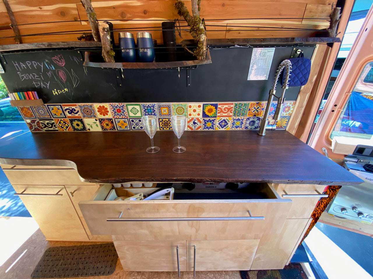 This RV rental features a cozy kitchen with wood counters, colorful tiles, and a compact stove, perfect for tiny living adventures.