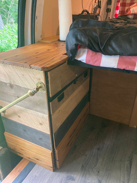 An inviting RV rental interior: custom wooden cabinetry, a cozy bed, and a durable laminate floor for comfortable van life.