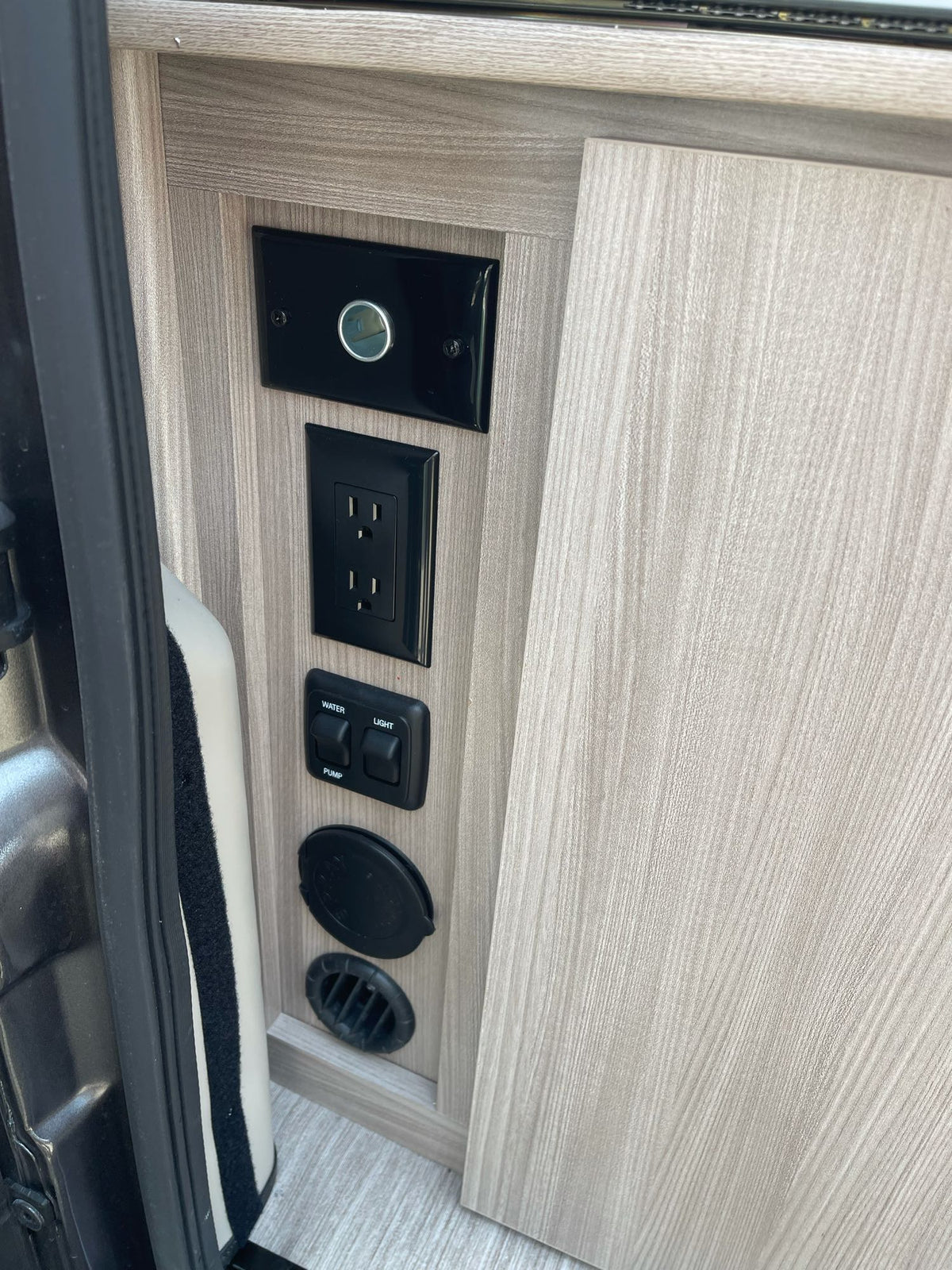 RV rental interior panel: electrical outlet, water pump & light switches, and vents on wood grain. — photo 18