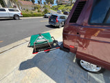 A burgundy RV rental van with a green Cuisinart grill mounted on a rear hitch carrier, ready for outdoor cooking.
