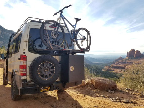 White Mercedes Sprinter rv rental van with a mountain bike & spare tire, parked at a breathtaking red rock overlook.