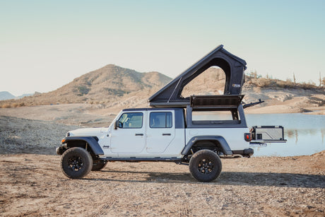 White Jeep Gladiator with rooftop tent & ARB fridge, an ideal RV rental for overlanding by the lake.