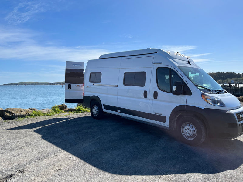 A white Winnebago Solis RV rental is parked by a scenic bay with its back door open, perfect for travel adventures. — photo 4