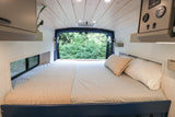 Cozy RV rental bedroom with a comfortable bed and stunning forest view from the rear doors.