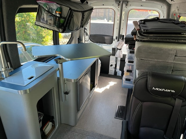 Spacious ModVans RV rental interior: This camper van features a compact kitchen with sink, adjustable table, and smart storage.