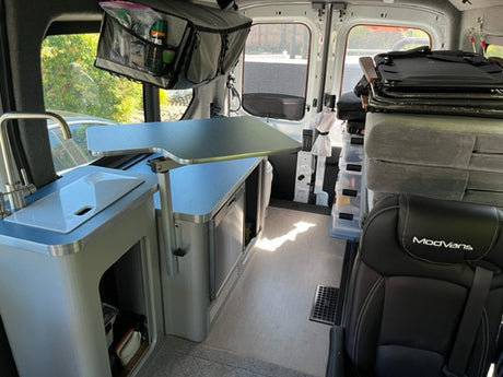 Spacious ModVans RV rental interior: This camper van features a compact kitchen with sink, adjustable table, and smart storage.