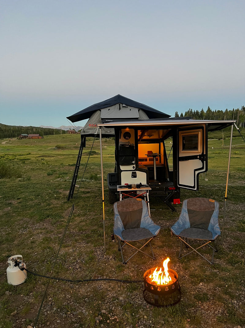 Twilight RV rental camping scene: a camper trailer with a rooftop tent, chairs, and a propane fire pit. — photo 3