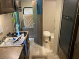 Inside an RV rental, showing the compact kitchen with sink, stove, microwave, a convertible bed, and a small bathroom.