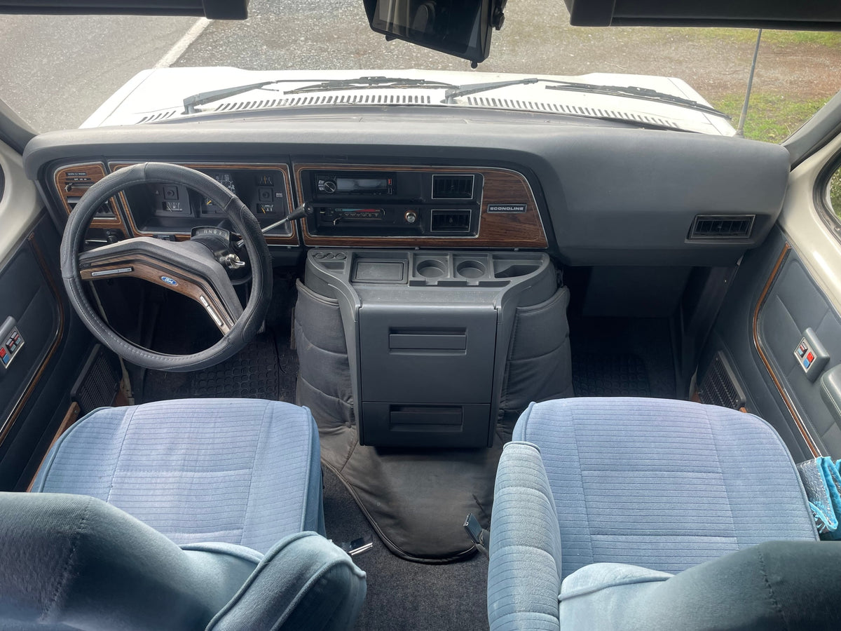 View from inside a classic Ford Econoline rv rental, highlighting its dashboard, steering wheel, and light blue front seats. — photo 6