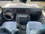 View from inside a classic Ford Econoline rv rental, highlighting its dashboard, steering wheel, and light blue front seats.