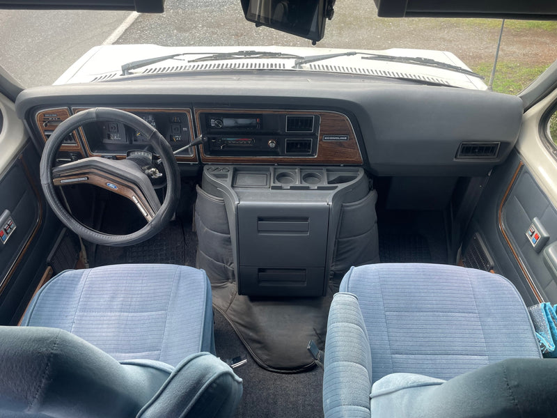 View from inside a classic Ford Econoline rv rental, highlighting its dashboard, steering wheel, and light blue front seats. — photo 6