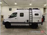 Silver Mercedes-Benz Sprinter rv rental camper van with roof rack, ladder, and off-road tires, charging indoors.