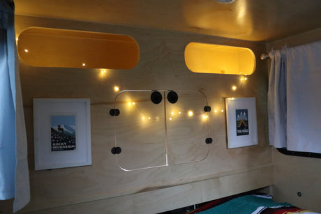 Cozy RV rental interior features wooden walls, ambient lights, overhead storage, and framed art for a homey feel.