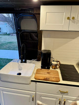 RV rental's sleek kitchen features a vessel sink, black faucet, coffee maker, induction cooktop, and white cabinetry.