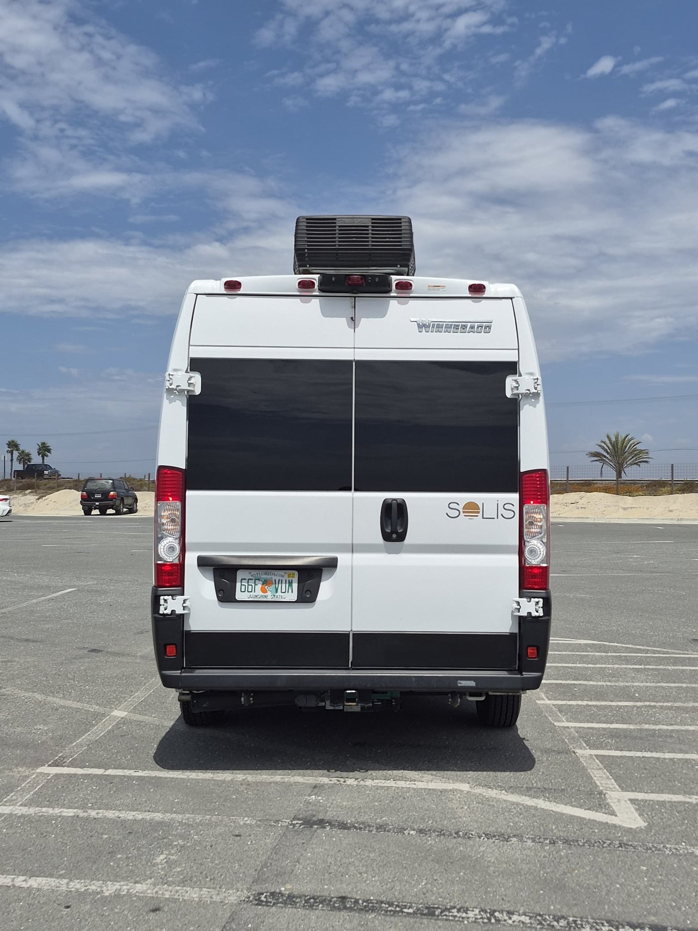  parked in a bright outdoor lot.|White Winnebago Solis RV rental parked in a sunny coastal lot with palm trees — photo 7