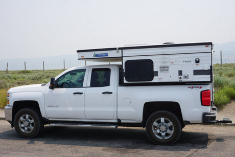 White Chevy 2500HD pickup with Four Wheel Hawk pop-up truck camper. Explore the outdoors with this RV rental!