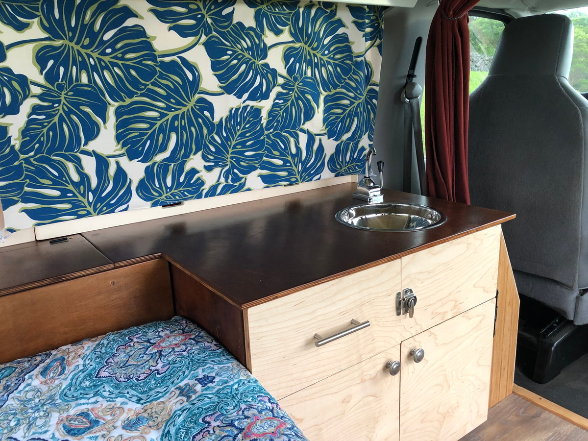 Custom **RV rental** interior: wooden kitchenette with sink, a cozy bed, and vibrant tropical leaf curtains. — photo 2
