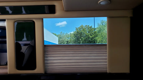 Luxury RV rental interior with a bright window view of sky & trees, a partially drawn blind, and a reflective screen.