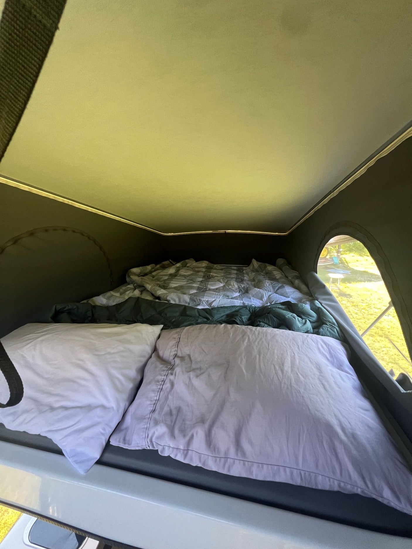 Inside an RV rental pop-top camper: a cozy bed with pillows and blankets, offering a comfortable sleeping space for travel.
