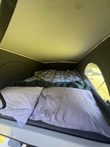 Inside an RV rental pop-top camper: a cozy bed with pillows and blankets, offering a comfortable sleeping space for travel.